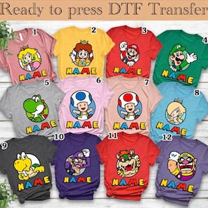 May include: A collection of twelve colorful t-shirts featuring various cartoon characters. Each shirt displays a character's image within a circle, with the word "NAME" below. The text "Ready to press DTF Transfer" is at the top.