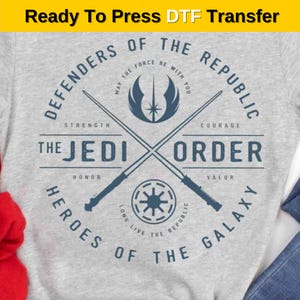 May include: A gray t-shirt with a blue and white graphic design featuring the text "Defenders of the Republic", "The Jedi Order", and "Heroes of the Galaxy". The graphic also includes a lightsaber, a star, and a symbol of the Republic.