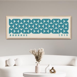 May include: A white couch and a white coffee table with a teal framed print on the wall behind it. The print has a geometric pattern and the text "BAUHAUS 1919".