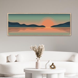 May include: A framed landscape art print featuring a sunset over a body of water. The artwork showcases a gradient of colors, including orange, teal, and navy blue. The print is displayed in a light-colored wooden frame, suitable for home decor.