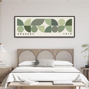 May include: A rectangular wall art print in a black frame featuring a geometric pattern of circles and semi-circles in various shades of sage and olive green on a cream background, with the text "BAUHAUS" on the left and "1919" on the right.