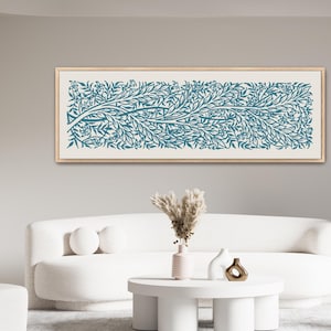 May include: A framed teal and white botanical print hangs above a white sofa. The artwork features a stylized tree branch with leaves and small flowers. The room has a modern, minimalist design with a white coffee table and chair.