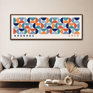 May include: A framed Bauhaus art print featuring a geometric pattern of orange, blue, and teal semi-circles on a cream background. The word "BAUHAUS" is printed in blue, and "1919" in orange.