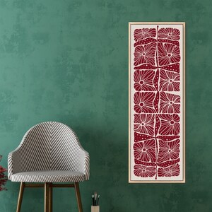 May include: A vertical wall art print with a red and white geometric pattern of stylized flowers. The print is framed in a natural wood frame and is hanging on a green wall.