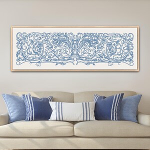 May include: A framed artwork featuring a blue and white floral design hangs above a beige sofa with blue and white pillows. The artwork has a light wood frame. Two matching lamps sit on either side of the sofa.