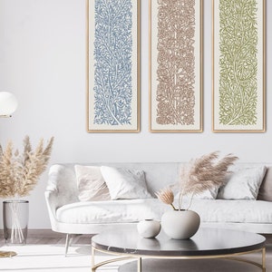 May include: Three framed prints of stylized floral patterns. The prints are in shades of blue, brown, and green. The prints are hanging on a white wall above a white couch with throw pillows.