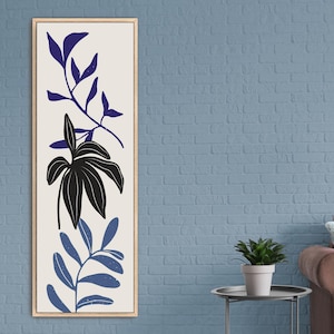 May include: A framed print of a stylized floral design with blue and black leaves on a white background. The print is hanging on a blue brick wall above a brown sofa.