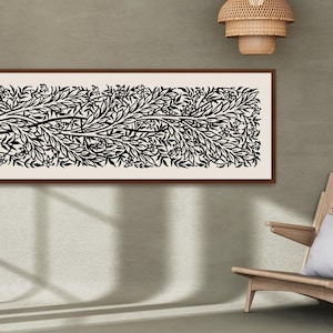 May include: A black and white line art print of a stylized tree with branches and leaves in a brown frame. The print is hanging on a light beige wall above a wooden chair with a white cushion.