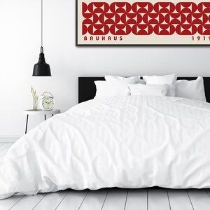 May include: A white bed with a white duvet cover and red and white geometric print artwork above the headboard. The artwork has the text "BAUHAUS 1919" printed on it.