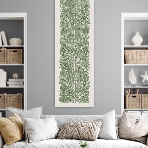 May include: A vertical canvas art piece featuring a detailed green botanical design on an off-white background. The artwork showcases a repeating pattern of leaves, berries, and vines, creating a nature-inspired aesthetic. The piece is displayed above a sofa in a living room setting.