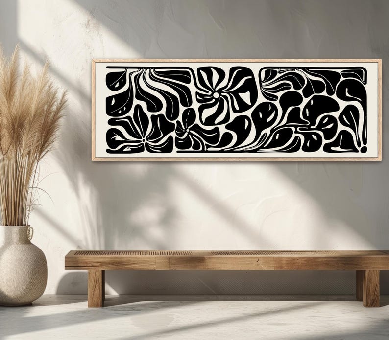 May include: A framed abstract art piece with a black and white floral design. The artwork features organic shapes and patterns, creating a modern aesthetic. The frame is a light wood color, and the artwork is displayed above a wooden bench.