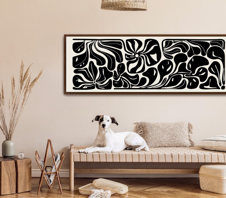 May include: A long, rectangular framed artwork with a black and white abstract design. The artwork features organic shapes and patterns. A dog is lying on a bench in front of the artwork.