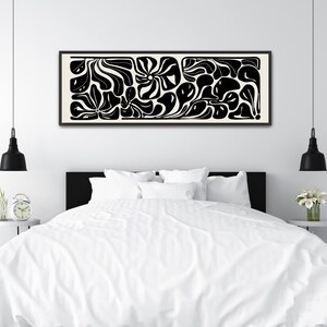 May include: Black and white abstract art print in a rectangular black frame. The artwork features organic shapes and flowing lines on a cream background. The print is displayed above a bed with white bedding.