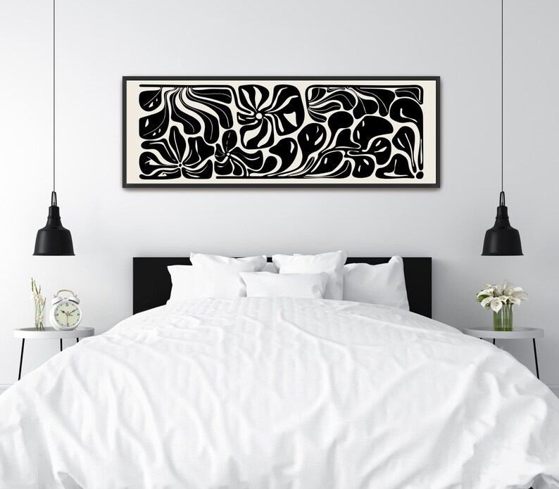 May include: Black and white abstract art print in a rectangular black frame. The artwork features organic shapes and flowing lines on a cream background. The print is displayed above a bed with white bedding.