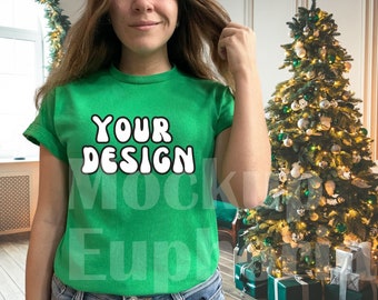 May include: A green t-shirt with the text "YOUR DESIGN" in white letters. The shirt is being modelled by a person with long brown hair. The person is standing in front of a Christmas tree.
