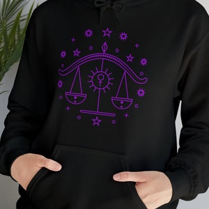 May include: Black hoodie with a purple outline of a Libra zodiac symbol with stars and a sun in the center.