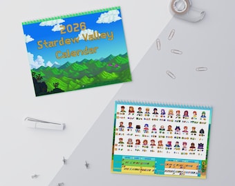 Könnte beinhalten: Ein spiralgebundenes Stardew Valley-Kalender 2026 mit blauem Himmel, Wolken und grünen Bergen. Der Kalender zeigt Charakterillustrationen und ein monatliches Layout. Bürobedarf ist verstreut.