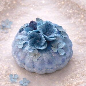 Handmade blue floral bath bomb with sparkling texture placed on lace with pearls, luxury bath gift set detail.