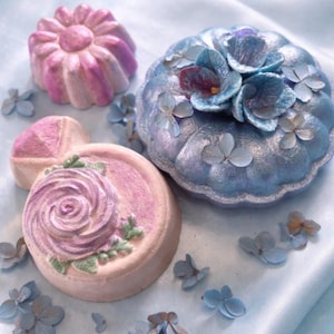 Handmade floral bath bombs in pastel pink and blue from a luxury spa gift box arranged on a soft romantic background.