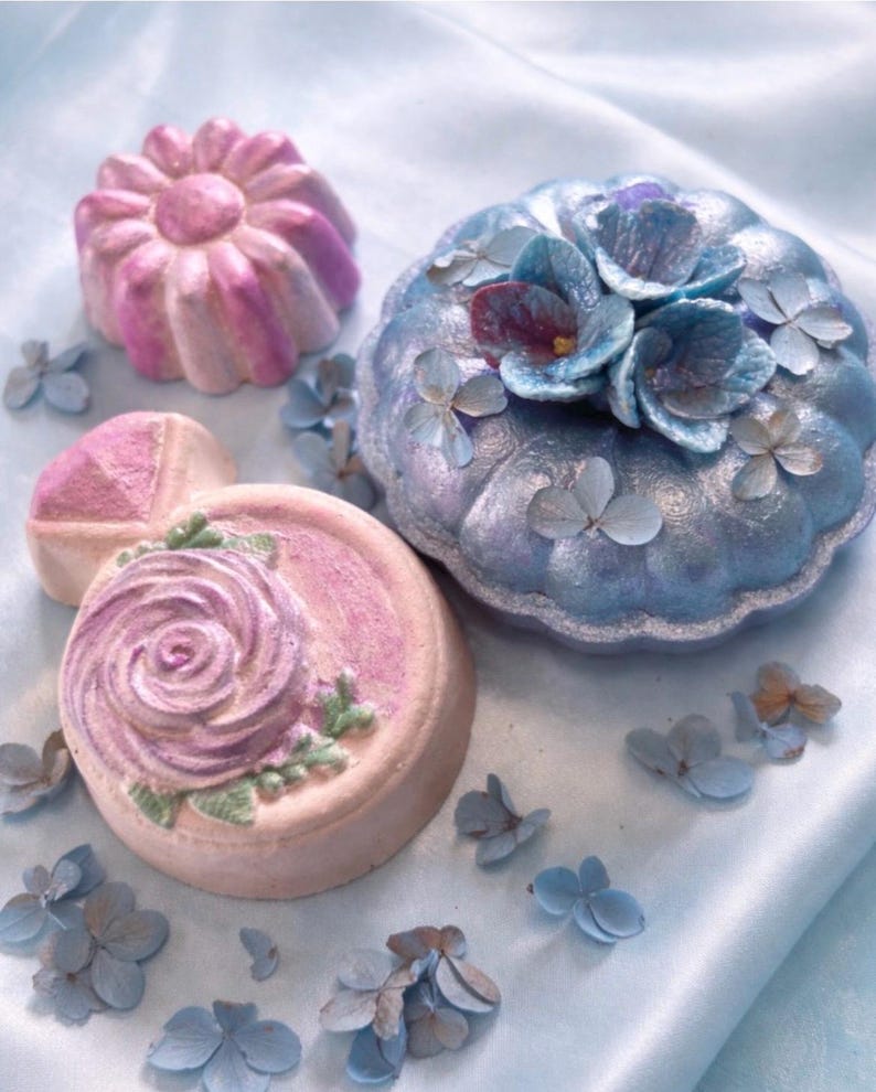 Handmade floral bath bombs in pastel pink and blue from a luxury spa gift box arranged on a soft romantic background.