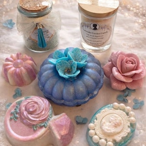 Luxury spa gift set items including bath salts, candle, bath bombs and handmade soaps arranged on lace with pearls.
