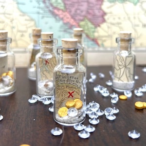 May include: Six small glass bottles filled with sand, seashells, and gold coins. Each bottle contains a rolled up piece of paper with a map printed on it. The bottles are arranged on a wooden surface with clear plastic gems scattered around them.