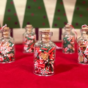 May include: Five small glass bottles filled with Christmas-themed polymer clay pieces. The bottles have cork stoppers and are filled with red, green, and white candies, gingerbread men, and Santa Claus shapes. Each bottle has a red and white string attached.
