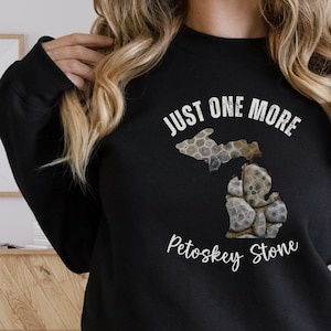 May include: Black sweatshirt with a white graphic of the state of Michigan made of Petoskey stones. The text "Just One More Petoskey Stone" is printed below the graphic.