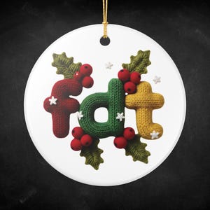 May include: A white ceramic Christmas ornament with the letters "fdt" in red, green, and yellow knitted designs. The ornament features holly leaves, red berries, and white snowflake accents, suspended by a gold string.