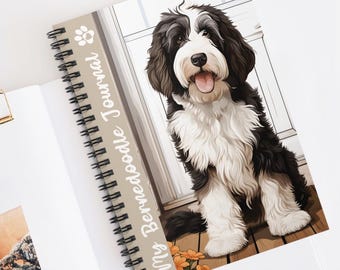May include: A spiral-bound journal featuring a black and white Bernedoodle dog illustration on the cover. The cover includes the text "My Bernedoodle Journal" in white script, a small paw print icon, and orange flowers at the bottom of the dog.
