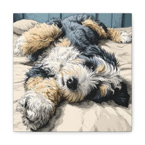 May include: A canvas print of a dog lying on its back, looking directly at the viewer. The dog has a mix of black, tan, and white fur. The background is a light beige, suggesting a bed or blanket.