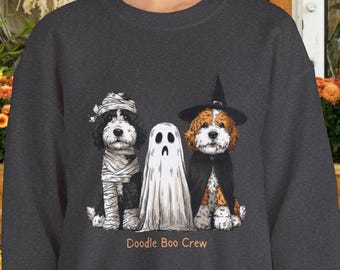 May include: A dark gray crewneck sweatshirt featuring a graphic of two dogs and a ghost. One dog is dressed as a mummy, the other as a witch with a black hat and cape. The ghost stands between them. The text "Doodle Boo Crew" is printed below.