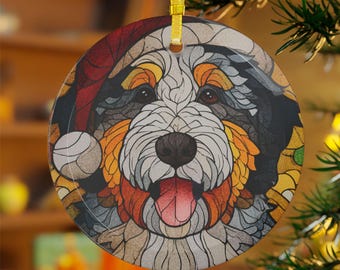 May include: Round Christmas ornament featuring a colorful, stylized dog wearing a Santa hat. The dog has a black nose, brown eyes, and a red tongue. The ornament is trimmed with a gold ribbon for hanging.