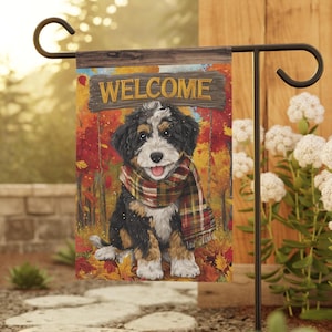 May include: A rectangular garden flag featuring a black, white, and tan puppy wearing a plaid scarf. The puppy sits in a forest with autumn leaves. Above the puppy, a wooden sign displays the word WELCOME in yellow capital letters.