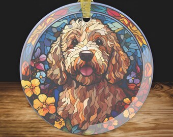 May include: Round glass ornament featuring a brown and tan dog with a stained-glass effect. The dog is surrounded by colorful flowers in shades of yellow, orange, blue, and purple. A gold ribbon is attached for hanging.