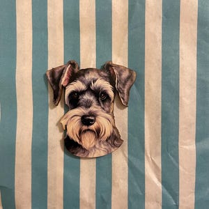 Könnte beinhalten: Holzausschnitt in Form eines Schnauzer-Hundes mit detailliertem Gesicht, grau-schwarzem Fell und langem, weißem Bart. Der Ausschnitt befindet sich vor einem Hintergrund aus blau-weißen vertikalen Streifen.
