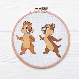 May include: Cross-stitch embroidery hoop featuring two cartoon chipmunks, one brown and one tan, with white accents. The chipmunks are smiling and looking at each other.