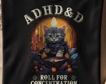 May include: Black t-shirt with a graphic of a gray kitten in a dark blue cloak, seated on a table. The text "ADHD & D" is above the kitten, and "ROLL FOR CONCENTRATION" is below. The design has a fantasy theme.