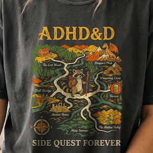 May include: A charcoal gray t-shirt featuring a fantasy map graphic with the text ADHD&D at the top and SIDE QUEST FOREVER at the bottom. The map depicts a raccoon adventurer, a dragon, a treasure chest, and various labeled locations.