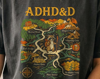 Puede incluir: Una camiseta gris carbón con un gráfico de mapa de fantasía con el texto ADHD&D en la parte superior y SIDE QUEST FOREVER en la parte inferior. El mapa muestra un mapache aventurero, un dragón, un cofre del tesoro y varias ubicaciones.
