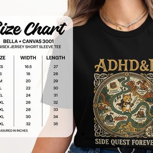 Puede incluir: Una camiseta negra de manga corta con un gr&aacute;fico de un gato aventurero en un mapa con el texto ADHD&D y SIDE QUEST FOREVER. A la izquierda se ve una tabla de tallas que enumera anchos de 16,5 a 32 y largos de 27 a 35.