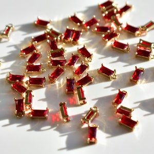 May include: A scattering of red and gold rectangular-shaped charms with a small loop at the top. The charms are scattered on a white surface.