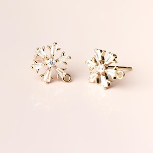 May include: A pair of gold snowflake earring findings with clear crystal accents. The findings have a loop on the back for attaching to earrings.