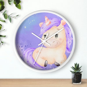 May include: A white clock with a purple and white unicorn design. The unicorn has a pink horn and a purple mane and tail. The clock face is a light purple with white clock hands and a white border.