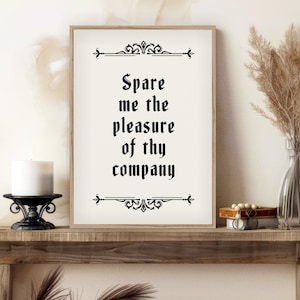 May include: A white framed print with black text that reads "Spare me the pleasure of thy company" in a decorative font. The print is on a wooden shelf with a candle and a vase of dried flowers.
