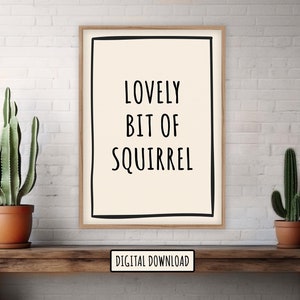 May include: A framed print with the text "LOVELY BIT OF SQUIRREL" in black on a cream background. The print is displayed on a wooden table with two potted cacti. The words "DIGITAL DOWNLOAD" are at the bottom.