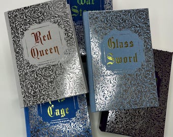 May include: Five hardcover books with silver and gold embossed designs. The titles are "War Storm", "Red Queen", "Glass Sword", "The Cage", and "The Broken Earth".