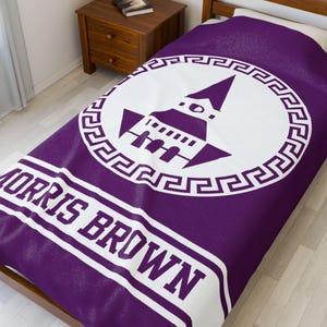 May include: A purple and white bedspread with the text "MORRIS BROWN" in white block letters. The bedspread features a white circular emblem with a building design and a Greek key border.