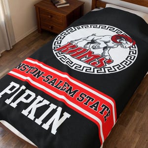 May include: Black blanket featuring the Winston-Salem State Rams logo in a white circle with a red and white border. The blanket also displays the text "WINSTON-SALEM STATE" and "PIPKIN" in white letters on a black background.