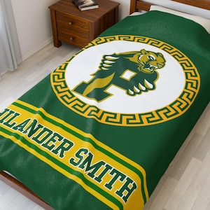 May include: Green and yellow fleece blanket with a white circle containing a green and yellow panther mascot with the letter "F" on its chest. The circle is surrounded by a yellow and gold Greek key pattern. The words "Islander Smith" are printed in a green and yellow stripe pattern at the bottom of the blanket.
